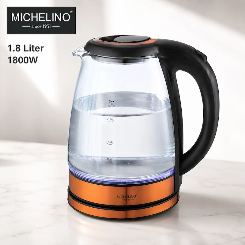 A 1.8 liter 1800W electric kettle by Michelino, featuring a clear glass body, black handle and lid, and an orange metallic base, shown on a light marble countertop with a white background.