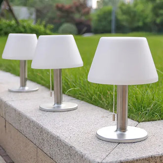 Three outdoor table lamps with white shades and metal bases on a stone ledge.