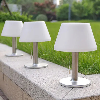 Three outdoor table lamps with white shades and metal bases on a stone ledge.